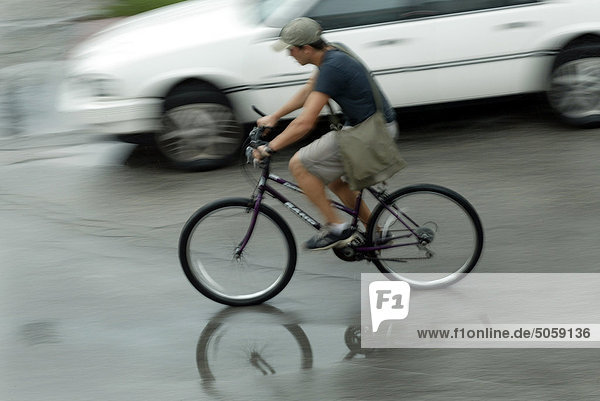 Junger Mann Fahren Fahrrads in einer nassen Straße