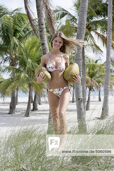 Frau am Strand tragen zwei Kokosnüsse