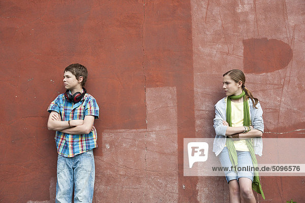 Junge mit Kopfhörer und Mädchen lehnen an einer Wand
