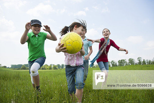 Vier Kinder spielen mit einem Fußball auf einer Wiese