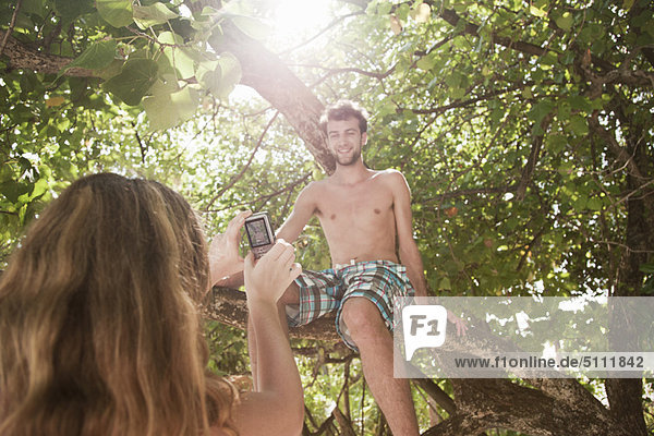 Woman taking photo of boyfriend in tree
