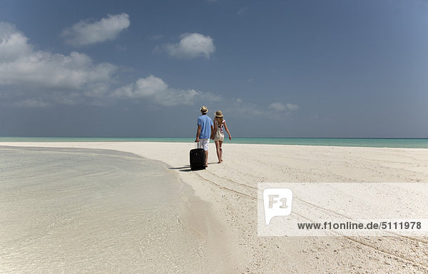 Couple rolling luggage on beach