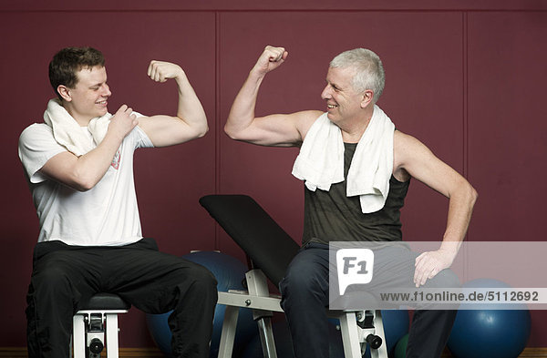 Father and son flexing muscles in gym