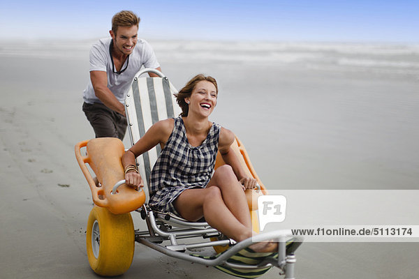 Man pushing girlfriend in cart on beach