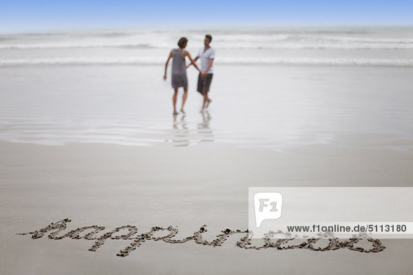 ‘Happiness’ in sand with couple on beach