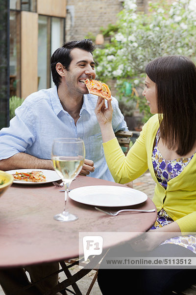Couple feeding each other pizza outdoors