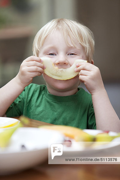 Junge spielt mit Melonenscheibe am Tisch