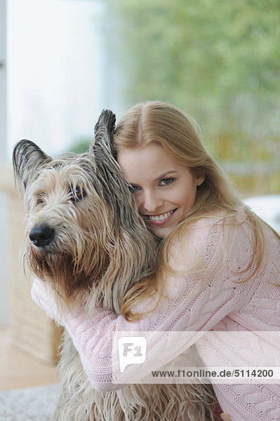 Lächelnde Frau umarmt Hund zu Hause