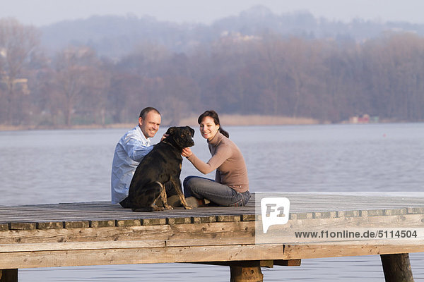 Couple petting dog on jetty over lake