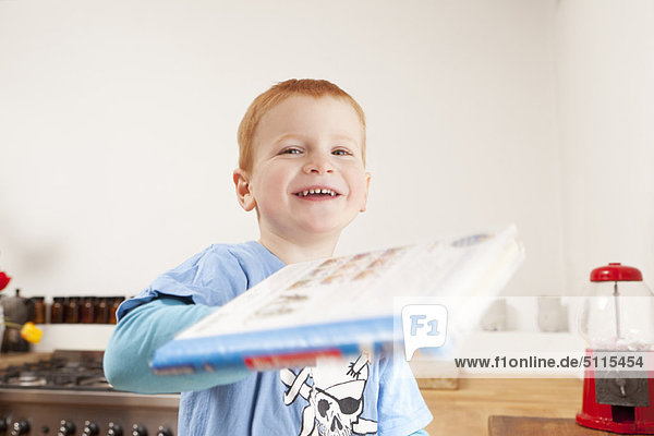 Lächelnder Junge mit Buch in der Küche