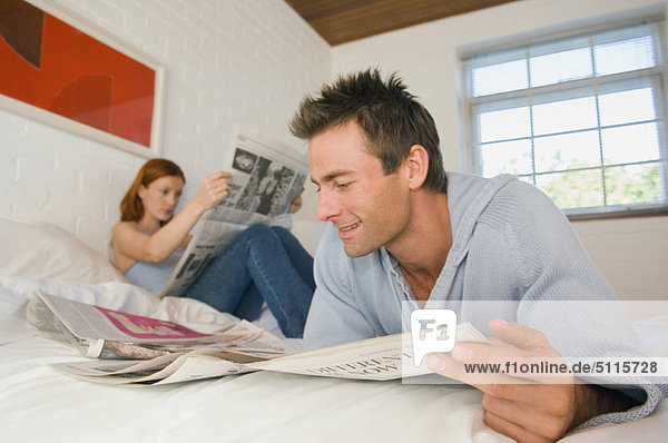 Couple reading newspaper in bed