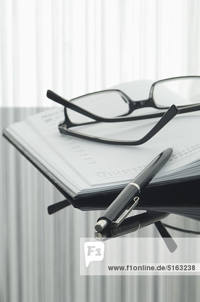 Close up of notebook  pen and spectacles with reflection on table