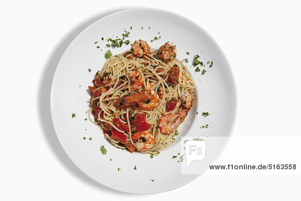 Nahaufnahme von Spaghetti mit in Chili-Öl gebratenen Scampis  Tomaten und Kräutern auf weißem Hintergrund