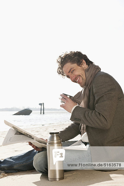 Mid adult man drinking and reading newspaper near Elbe river  smiling  portrait