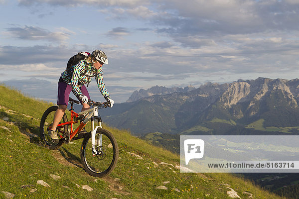 Austria  Tyrol  Spitzstein  Young woman mountainbiking on slope with Kaiser mountains in background