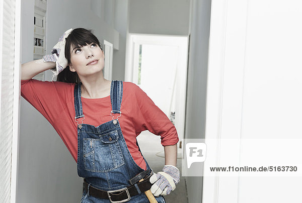 Young woman with hammer leaning on wall at renovating apartment