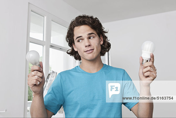 Junger Mann mit normalen und energiesparenden Glühbirnen in der renovierten Wohnung