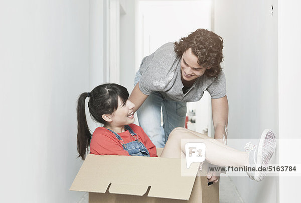 Junge Frau im Karton und Mann schiebt sie in die renovierende Wohnung