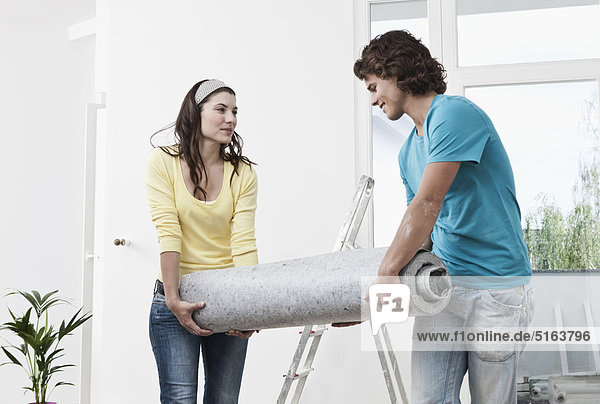 Deutschland  Köln  Junges Paar mit Teppich in renovierter Wohnung