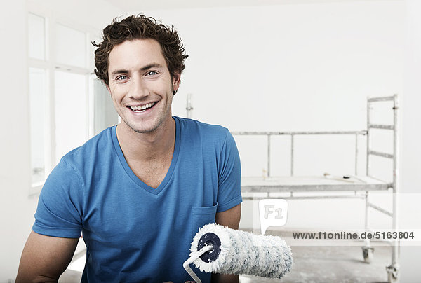 Nahaufnahme eines jungen Mannes mit Farbroller in der renovierenden Wohnung  Portrait  lächelnd