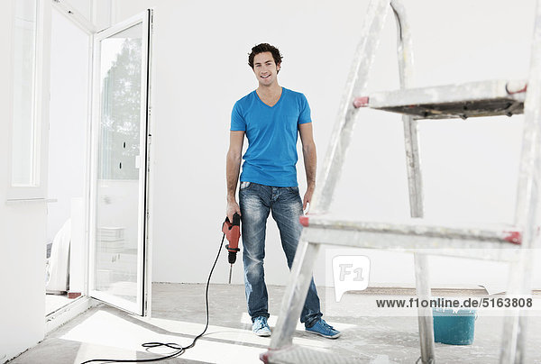 Junger Mann mit Elektrobohrer in renovierter Wohnung