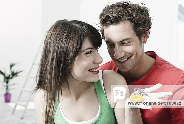 Germany  Cologne  Close up of young couple holding house keys in renovating apartment  smiling