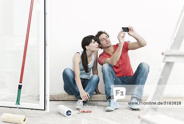 Deutschland  Köln  Junges Paar beim Betrachten von Handybildern in der renovierten Wohnung