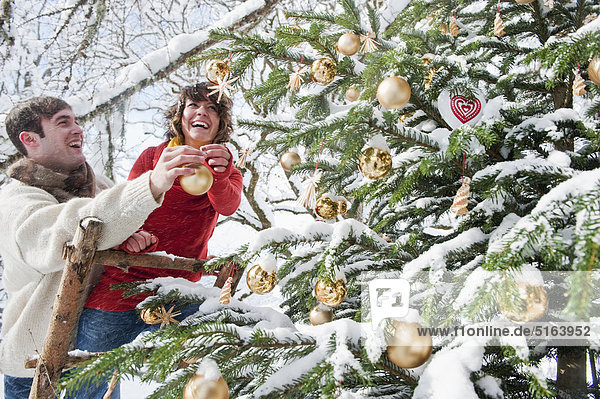 Österreich  Salzburger Land  Flachau  Junger Mann und Frau schmücken Weihnachtsbaum im Winter