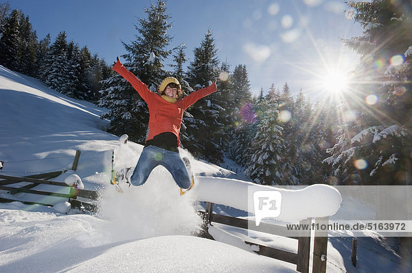 Austria  Salzburg Country  Flachau  Young woman wearing snow shoes jumping in snow