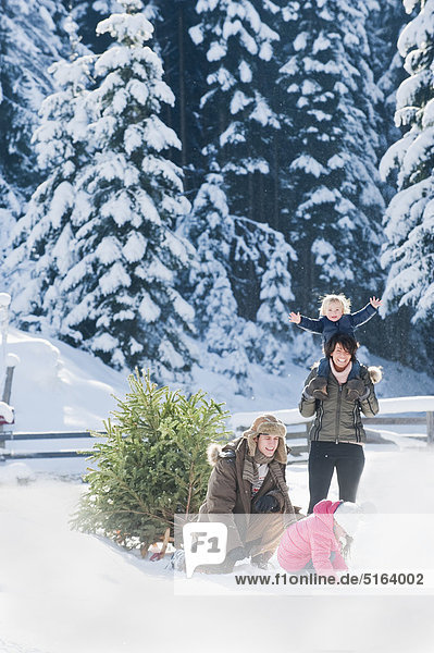 Österreich  Salzburger Land  Flachau  Blick auf die Familie mit Weihnachtsbaum und Schlitten im Schnee