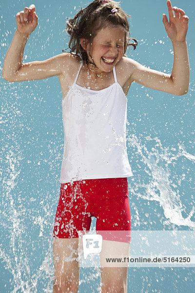 Germany  Girl jumping in splash of water against blue background