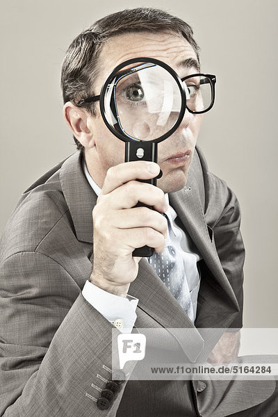 Close up of mature businessman looking through magnifying glass against grey background