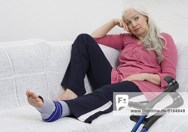 Frau mit Verband auf dem Sofa neben Krücken
