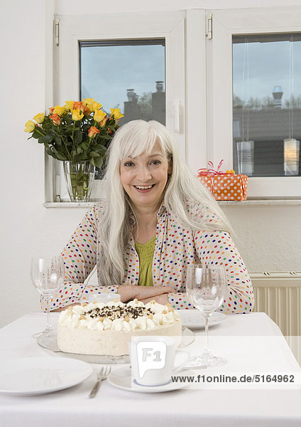 Woman sitting at dining table with cake  flowervase and present  smiling  portrait