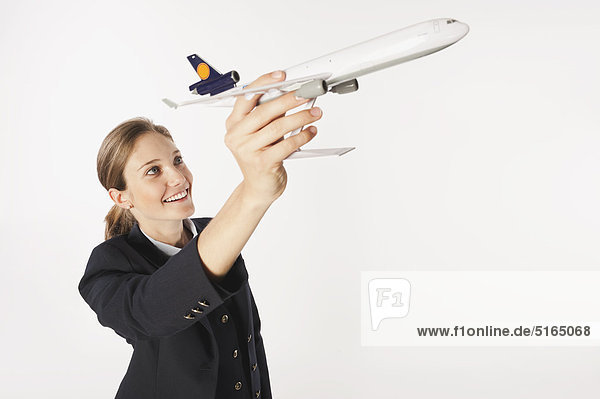 Junge Flugbegleiterin mit Modellflugzeug vor weißem Hintergrund  lächelnd  Portrait