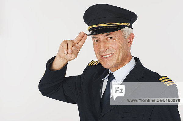 Nahaufnahme eines älteren Flugkapitäns  der vor weißem Hintergrund salutiert  lächelnd  Portrait