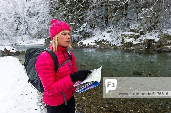 Woman map reading by snowy riverside.
