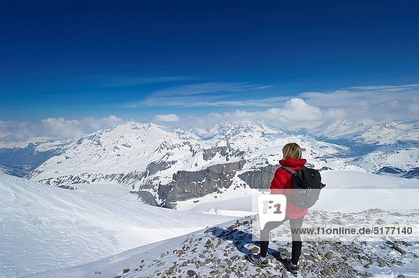 A women hiking in high snow covered mountains looks at view