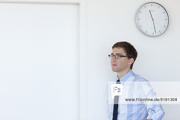 Businessman standing under office clock