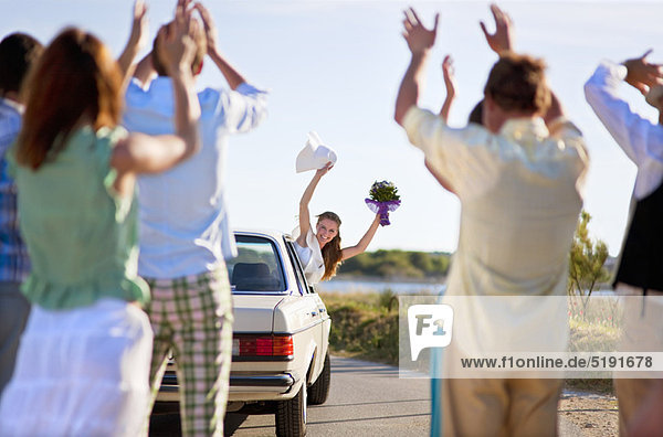 Bride waving to wedding party from car