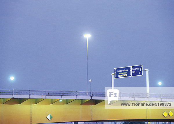 Beleuchtung und Hinweisschilder einer Straßenbrücke  abends