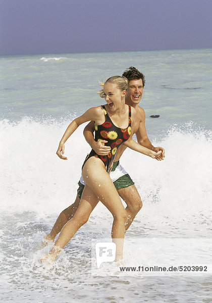 Paar  laufen am Strand durchs flache Wasser