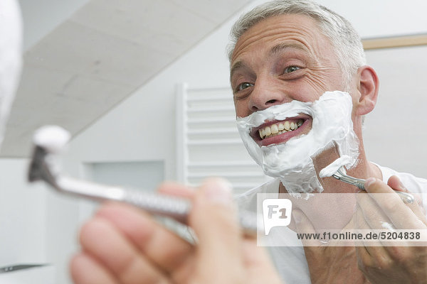 Mann rasiert sich nass in Badezimmerspiegel  lacht