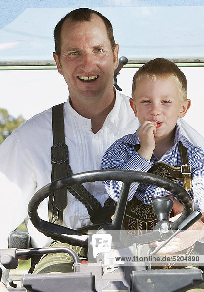 Vater mit kleinem Sohn in Lederhosen auf Traktor