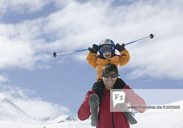 Kleiner Junge sitzt mit Skiern bei Vater auf Schultern