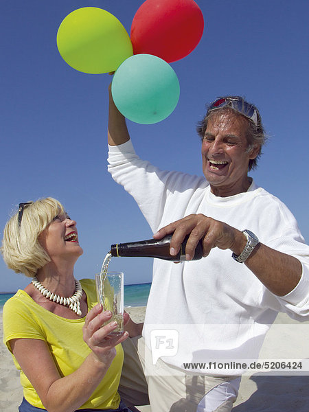 Älteres Paar feiert mit Sekt und Luftballons am Strand