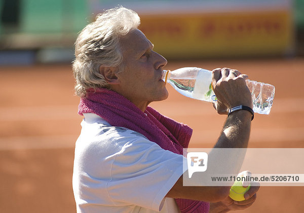Älterer Mann als Tennisspieler  trinkt Wasser