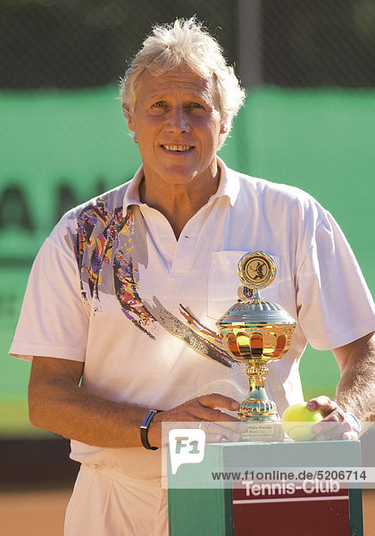 Älterer Mann als Tennisspieler mit Siegerpokal