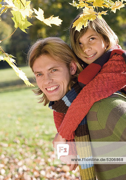 Vater mit Tochter auf dem Rücken in herbstlichem Park  Halbporträt