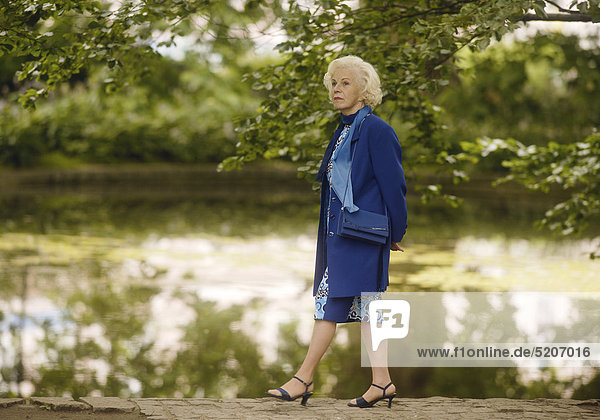 Seniorin spaziert allein in Park an Teichufer